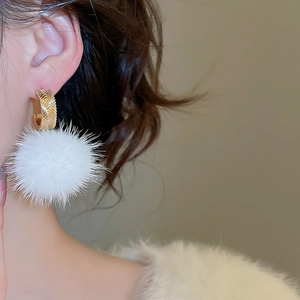 Close-up of elegant gold hoop earrings with soft white plush balls for winter style