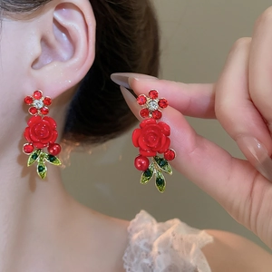 Detail of red rose earrings with green leaves and crystals on model and hand