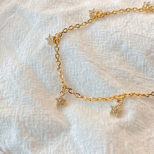 Macro detail of gold flower pendants with white crystals on a delicate chain link