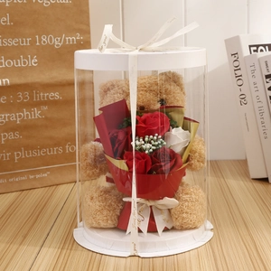 Close-up of a light brown teddy bear holding soap roses in a round transparent gift box