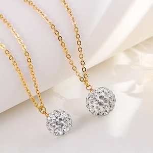 Close-up of gold chain necklaces featuring round crystal pavé ball pendants and shiny details