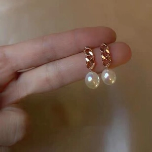 Detail of baroque pearl drop earrings with rose gold curb links held for size scale