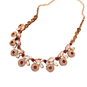 Vintage style gold necklace with red and pink zircon crystals on a white background