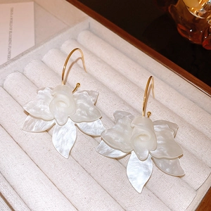 Detailed close-up of cream resin flower earrings with gold hooks on beige velvet