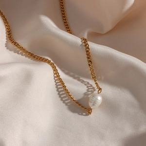 Detailed close-up of a golden Cuban chain necklace featuring a white baroque pearl pendant