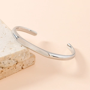 Minimalist silver stainless steel open bangle displayed on a natural stone base