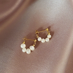 Close-up of elegant C-shaped earrings with white pearls and gold metal beads on silk