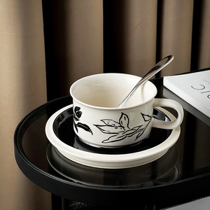 Detailed view of white ceramic coffee cup with hand-painted black leaf pattern and saucer