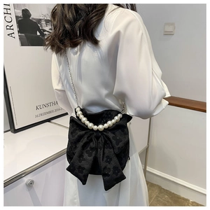 Detail of black bow shoulder bag with pearl chain shown on model in a minimalist room