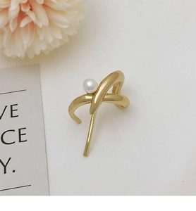 Detail of a golden crisscross hair clip featuring an elegant white pearl inlay
