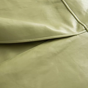 Detail showing the fine leather texture and precision stitching on the light green trench coat