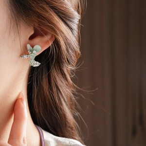 Detail of flower stud earrings with green stones and silver finish on ear