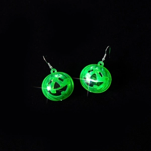 Close-up of green glowing pumpkin LED earrings for Halloween costume on dark background