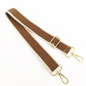 Detail of adjustable geometric F-pattern bag strap with gold metal buckle hardware