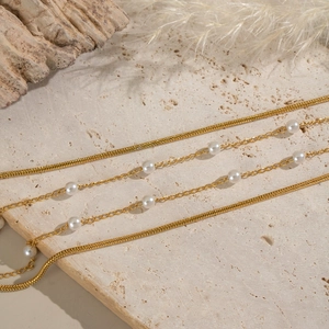 Detail of double-layer 18K gold plated necklace with pearls on a textured stone surface