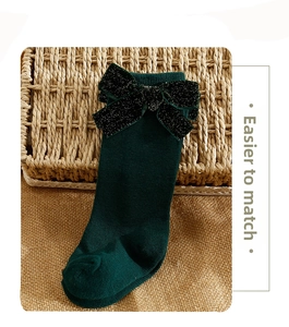 Detail of dark green knit socks with sparkling black bow on rustic background
