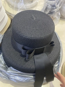 Detail view of black woven straw hat featuring a flat top and elegant long ribbon bow