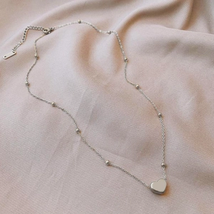Gros plan du pendentif cœur et de la chaîne à billes sur fond en tissu rose