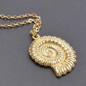 Macro detail of a golden conch shell pendant on a fine stainless steel chain necklace