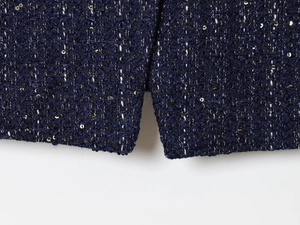 Detail von dunkelblauem Tweed-Stoff mit schimmernden goldenen Pailletten auf der Damenjacke