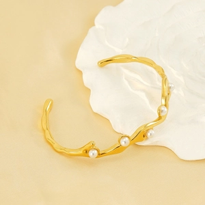 Dettaglio di un bracciale a onde placcato oro 18k con cinque perle su un piatto decorato