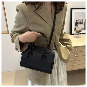 Minimalist black leather handbag with top handle and shoulder strap shown in a cafe setting