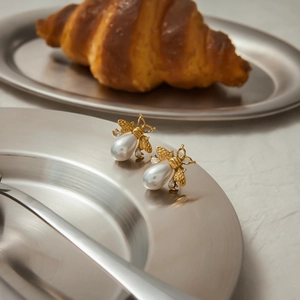 Detailed view of golden bee pearl earrings placed on an elegant silver plate