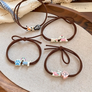 Detail of four brown elastic hair ties with cute resin cat and dog charms on linen