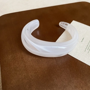 Nahaufnahme eines weißen Acryl-Armreifs mit Marmormuster auf braunem Lederhintergrund
