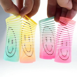 Close-up of hands holding four mini rainbow spring toys with colorful smiley faces