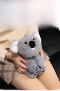 Close-up of a soft grey plush koala toy held by a person in a cozy home setting
