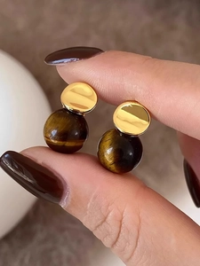 Macro shot of 18k gold plated tiger eye stone earrings held by fingers to show texture