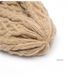 Dettaglio del berretto in maglia beige che mostra la finitura superiore e la trama a treccia