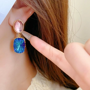 Close-up of vintage gold earrings with pink and blue gemstones worn by a model