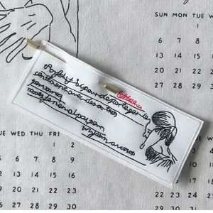 Artistic embroidered fabric brooch with female line art on a linen calendar background