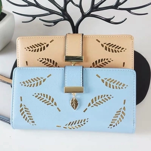 Detail of laser-cut leaf patterns and gold charms on light blue and beige faux leather wallets