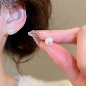 Macro detail of white round pearl earrings showing elegant luster on model earlobe