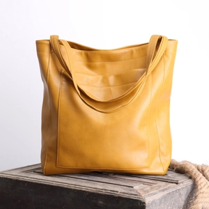 Grand sac cabas jaune en cuir huilé vintage avec poche posé sur une caisse en bois