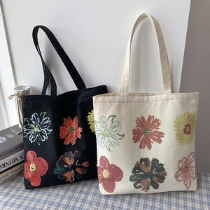 Canvas tote bags with colorful floral patterns in black and beige displayed on a blue cloth