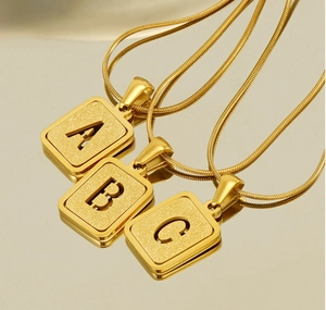 Détails macro des pendentifs lettres A B C ajourés en acier doré 18K sur chaînes serpent