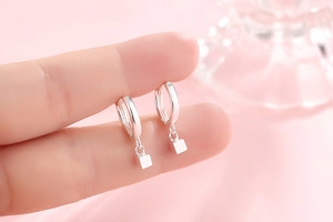 Close-up of minimalist s925 silver square dangle hoop earrings on a soft pink background