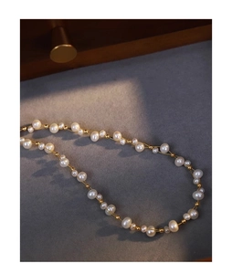 Macro view of woven baroque pearl necklace with golden metal beads on grey felt surface