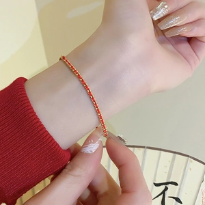 Detail of a thin red braided bracelet with gold beads worn against a festive background