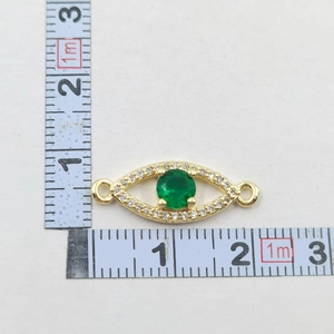 Detail of gold evil eye charm with green stone and clear stones next to a ruler