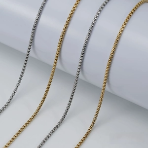 Detailed view of 18K gold and silver stainless steel box chains on a white pedestal