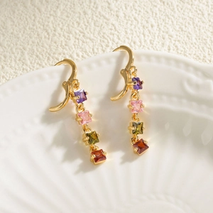 Long gold earrings with four colorful square zircons on a white textured plate