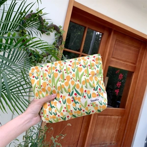 Close-up of canvas makeup bag featuring orange tulip prints and a woven brand label