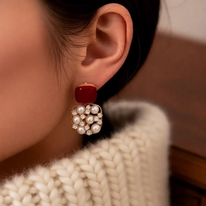Detail of 18k gold plated pearl and red square earrings worn by a model in natural light