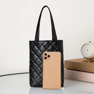 Detailed macro view of a black quilted mini tote bag next to a gold smartphone for scale