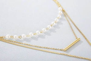 Close-up of layered gold necklace with white pearls and a minimalist metal bar pendant